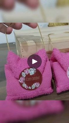 two pink knitted baby booties being held up by someone's hand with the tag on them