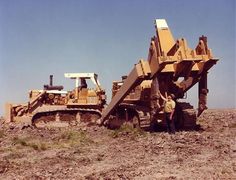 a man standing next to a bulldozer on top of a dirt covered field