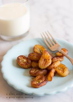 a blue plate topped with fried bananas next to a glass of milk and a fork