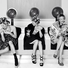 black and white photograph of three women sitting on a bench with hair dryers in their ears