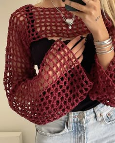 a woman is wearing a red crochet sweater and holding a cell phone in her hand