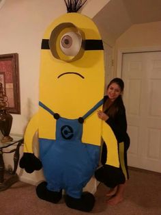 a woman standing next to a giant yellow and blue toy character in a living room