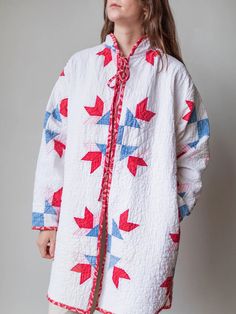 a woman standing in front of a wall wearing a white coat with red and blue stars on it