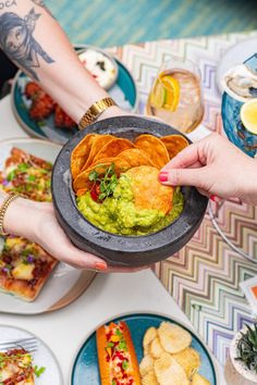 two hands holding a bowl filled with guacamole and tortilla chips