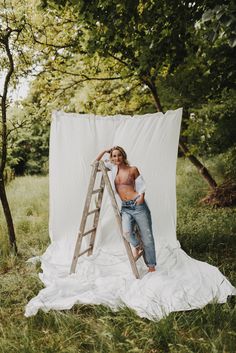 a man standing on top of a ladder next to a white tarp in the woods