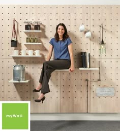 a woman sitting on top of a wooden shelf in front of a pegboard wall