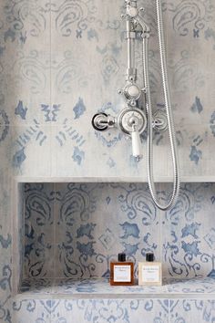 a bathroom with blue and white wallpaper has a shower head, soap dispenser, and mirror