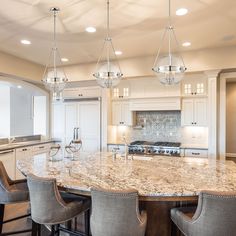 a large kitchen with marble counter tops and white cabinets, along with bar stools