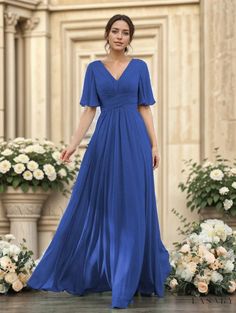 a woman in a long blue dress standing on a stage with flowers and greenery behind her