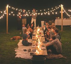 a group of people sitting around a long table with lights strung across the entire area