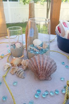 seashells and sand in glass vases sitting on a table with blue beads