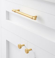 two brass handles on white drawers in a bathroom