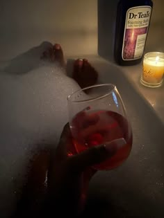 a person is holding a wine glass in the bathtub with soap and candles nearby