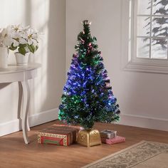 a small christmas tree with blue lights and presents on the floor in front of it