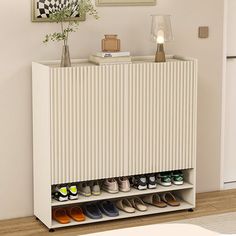 a white cabinet with several pairs of shoes on it in front of a wall mounted painting