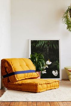 a yellow chair sitting in front of a painting on the wall next to a potted plant