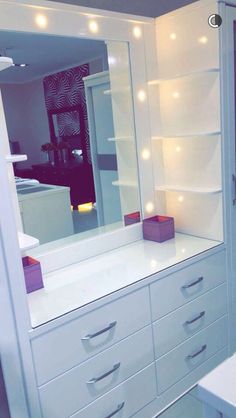 a white dresser sitting next to a bathroom sink under a mirror with lights on it