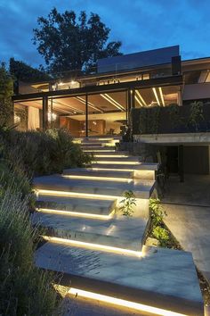 the stairs are lit up at night in front of a modern house with large windows