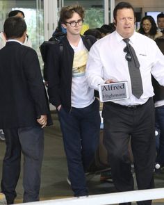 two men in business attire walking through an airport with luggage and people looking at them