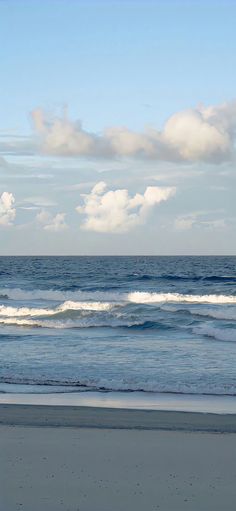 a person walking on the beach with a surfboard in hand and clouds in the background