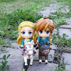 two figurines are standing next to each other on the ground in front of some grass