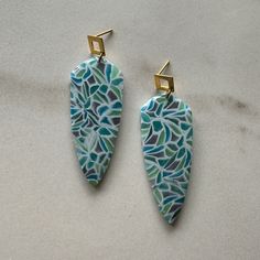 two blue and green earrings with gold ear clips on top of a white countertop