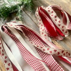 red and white ribbon with hearts on it sitting on a wooden table next to greenery