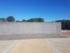 an empty parking lot in front of a wall with trees and blue sky behind it