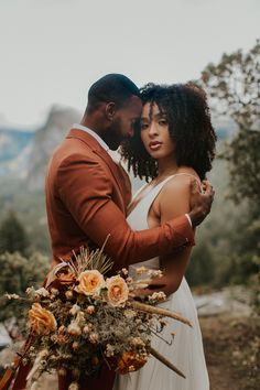 a man and woman standing next to each other in front of some trees with flowers