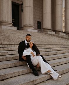 a bride and groom sitting on the steps of an old building in front of columns