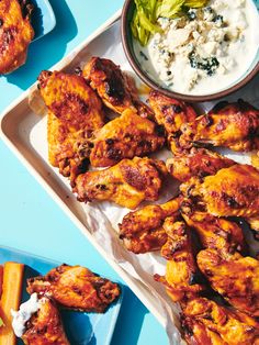 some chicken wings are sitting on a plate next to other foods and dips in bowls