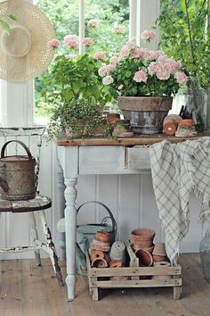 an old table with potted plants on it in front of a window and some chairs