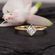 an engagement ring with a princess cut diamond on it and a flower in the background