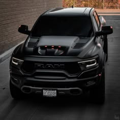 the front end of a black truck parked in a parking lot next to a brick wall