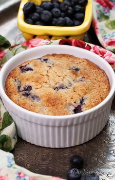 a blueberry cobbler in a white dish on a floral tablecloth next to two yellow dishes