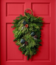 a christmas wreath hanging on a red door with pine cones and evergreens around it