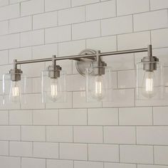 a bathroom light with five lights on the wall and white brick walls behind it,