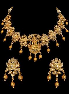 Traditional Indian temple bridal jewelry with stunning pearl stone-setting on a gold plated necklace & earrings. This temple choker jewelry set is elaborated with a goddess motif design pendant, making it one of a kind. Gold plated choker necklace with goddess engraved & floral design adorn this bridal neckpiece.  Stunning golden ball drops on this jewelry set is sure to make you feel like a million bucks with their elaborating handcrafted design. This short necklace set comes along with a beaut Diwali Gold Pearl Necklace With Intricate Design, Gold Pearl Necklace With Intricate Design For Diwali, Ceremonial Gold Pearl Necklace In Temple Jewelry Style, Ceremonial Gold Temple Jewelry Pearl Necklace, Gold Chandbali Pearl Necklace In Temple Style, Gold Chandbali Pearl Necklace In Temple Jewelry Style, Gold Jewelry Sets With Peacock Design For Festivals, Gold Temple Necklace With Stone Work For Diwali, Elegant Bridal Necklace For Navratri Puja