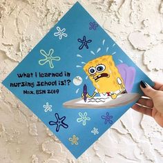 a hand holding up a blue graduation cap with an image of spongebob on it