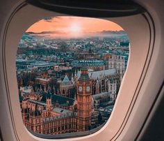 the view from an airplane window looking down on a city and clock tower at sunset