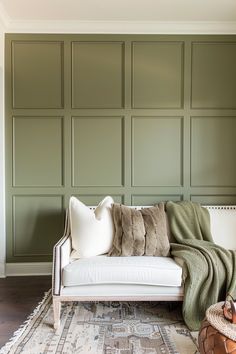 a white couch sitting on top of a wooden floor next to a wall covered in green paneling