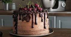 a chocolate cake topped with cherries on top of a wooden table