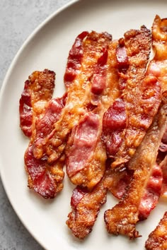 bacon strips on a white plate sitting on a gray table top next to a fork and knife