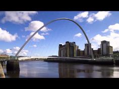 a bridge that is over some water with buildings and clouds in the sky behind it