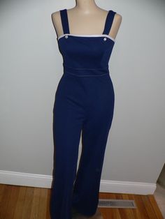 Great vintage 70's navy polyester knit jumpsuit. It is tight fitting and does have some stretch. The jumpsuit is accented with white across the top and stitches at the waist and blue buttons at the straps. The jumpsuit does up at the back with zipper and eyehook. The white jacket is accented with navy around the neckline and blues stitches. Ties at the front. No tags or labels. Measurements - shown on form unpinned with shoulders 14.5, bust 34, waist 23.5 and hips 34 Inches. Flat - bust 17 waist Fitted Overalls With Buttons For Workwear, Fitted Blue Jumpsuits And Rompers With Button Closure, Fitted Overalls With Button Closure, Fitted Overalls With Buttons, Navy Sleeveless Fitted Jumpsuits And Rompers, Vintage Fitted Blue Overalls, Vintage Blue Fitted Overalls, Blue Fitted Vintage Overalls, Fitted Retro Overalls