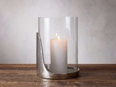 a lit candle in a glass container on a wooden table next to a metal object