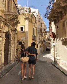 two people walking down an alley way with buildings in the background and one person holding a basket