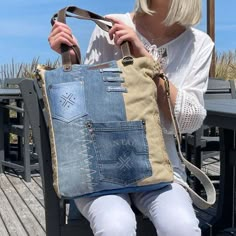 a woman is sitting on a bench holding a denim tote bag with holes in it