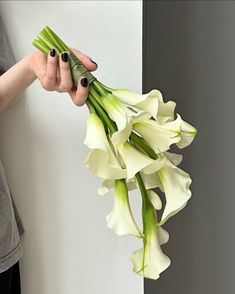 a woman holding flowers in her hand near a white wall and grey walls behind her