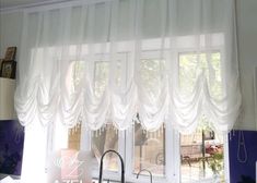 a kitchen window with white curtains hanging from it's side